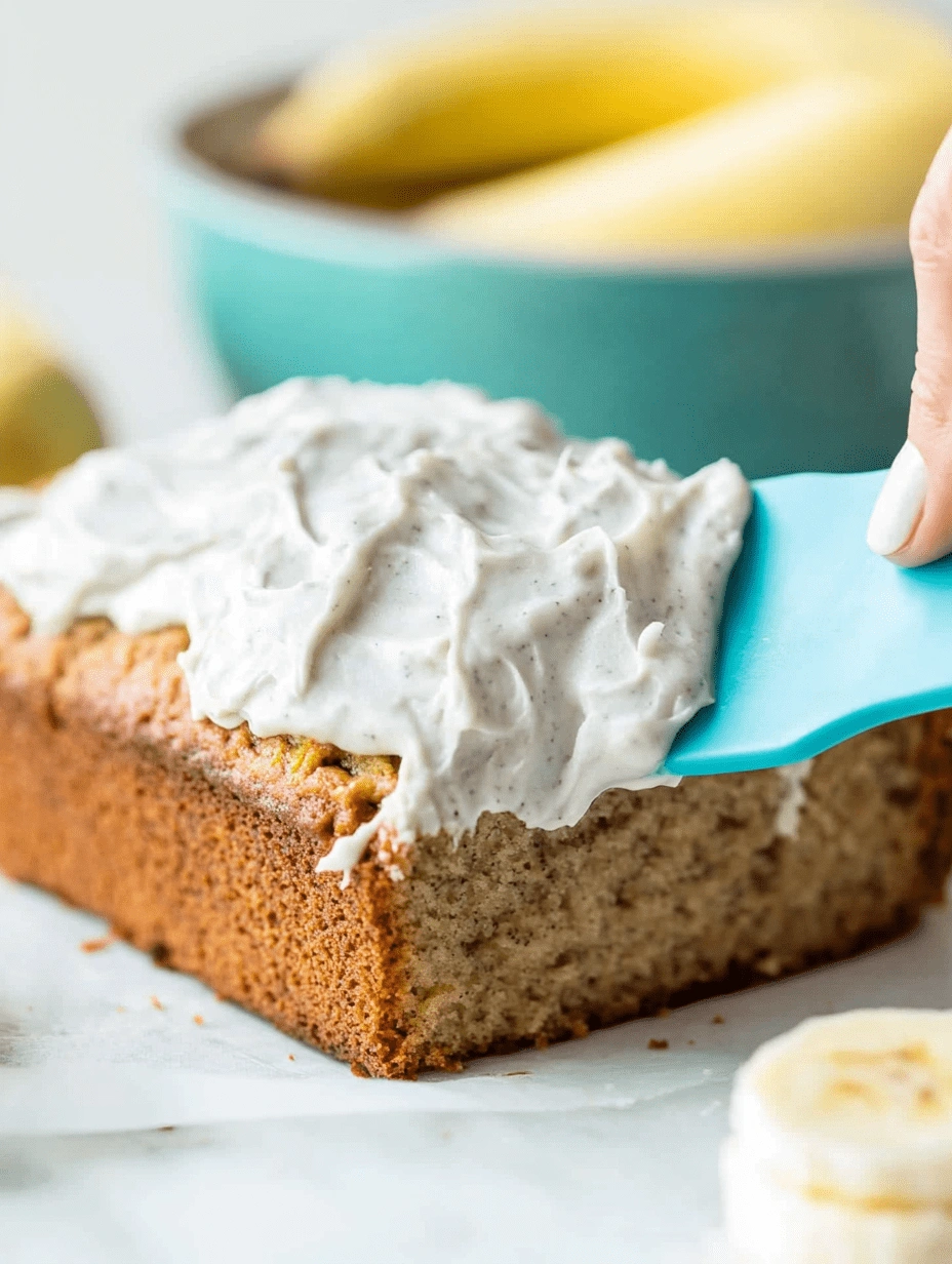 frosting-healthy-banana-cake-loaf Spreading creamy frosting over a healthy banana cake loaf with a blue spatula