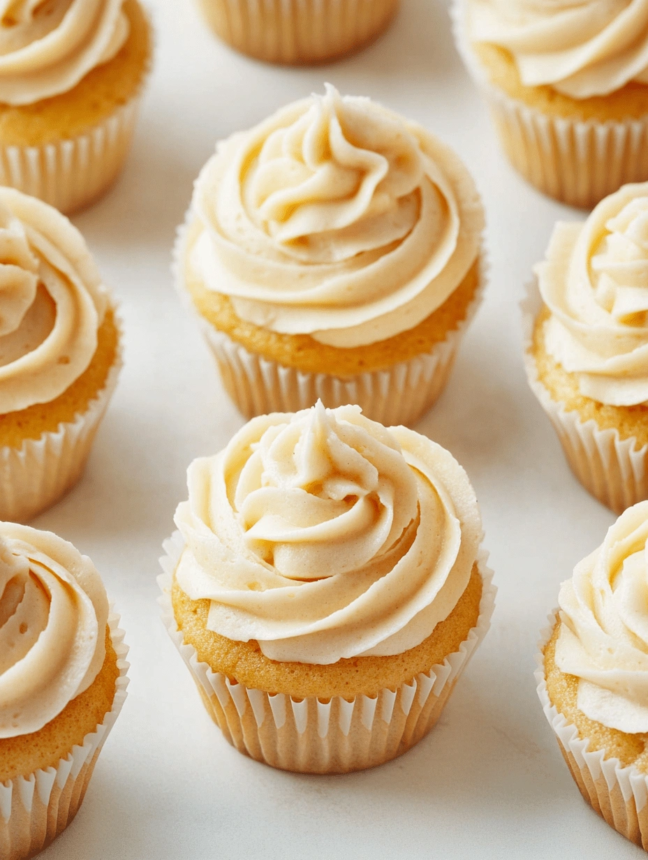 gluten-free-cupcakes-with-vanilla-frosting-top-view Top-down view of gluten-free cupcakes with piped vanilla frosting in white cupcake liners on a light background.
